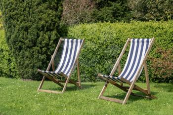 Two british deckchairs with striped cloth in an English garden in summer