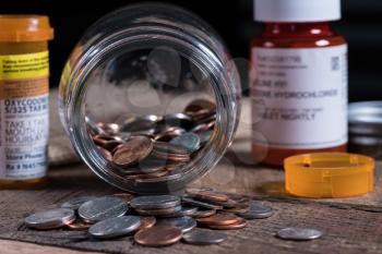 Poverty concept image with a few small coins remaining in a glass jar with opioid prescription drug bottle