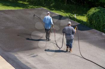 Workers applying blacktop sealer to asphalt street using a spray to provide a protective coat against the elements