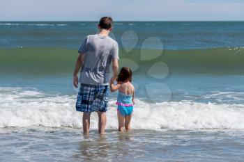 Back view of father and young girl facing the sea waves as concept for protection against future problems