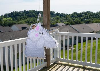 White pinata shaped like a unicorn hanging on the deck of modern home in USA for childs party