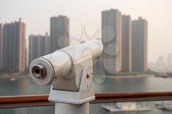 Metal optical telescope on deck of cruise boat looking misty buildings of Qingdao