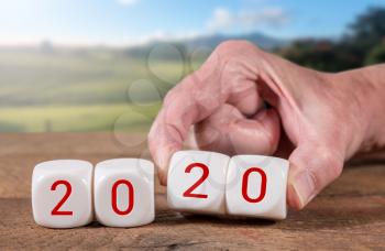 2020 spelled in cubes with man's hand turns over the dice on wooden table with sunlight on rural landscape