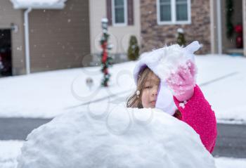 Young toddler girl playing in the snow and making a snowman