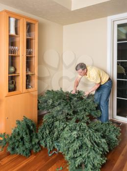 Senior adult man putting the various parts of an artificial xmas tree together to assemble the tree at Christmas