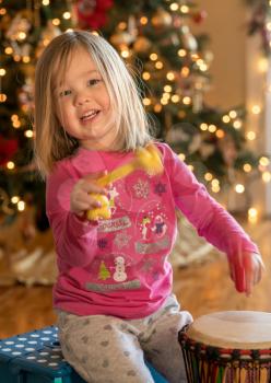 Young toddler girl playing an african drum with pieces of rope in front of christmas tree