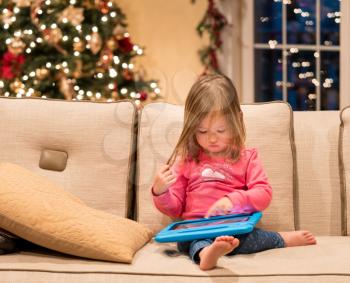 Young girl sitting at home on settee and using a child's tablet touch screen computer at xmas suggesting this was a present