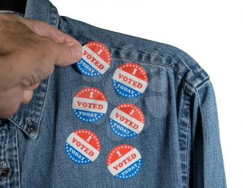 Hand placing multiple I Voted Today stickers on the blue denim working shirt collar for midterm elections in the USA with white background