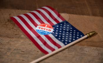 Narrow focus on I Voted Today sticker  for voters in the US elections with USA flag on rustic wooden table