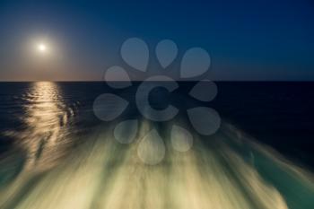 Moon rising over wake and waves of cruise ship at sea with concept of leaving or starting anew