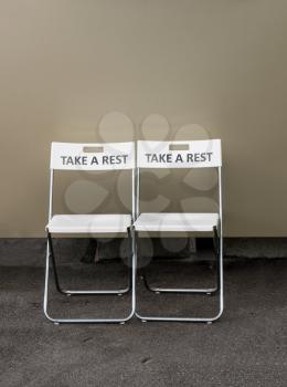 Pair of folding plastic chairs with the message Take a Rest engraved on the backrest