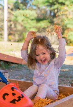 Young caucasian girl playing in the seeds from corn kernels and throwing them into the air at halloween pumpkin patch