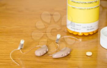 Macro close up of a matched pair of tiny modern hearing aids with nightly cholestrol drug and bottle on wooden bedside dressing table