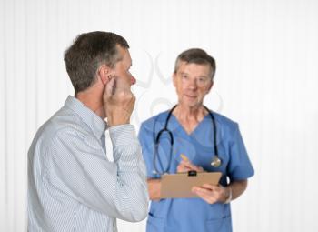 Senior male inserting hearing aid into his ear in consultation with his audiologist