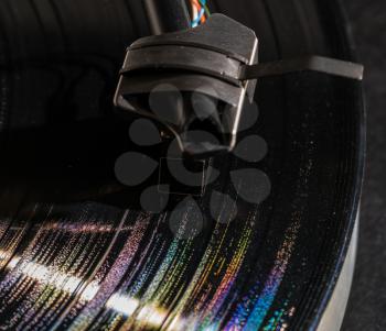 Rainbow colors from grooves in long playing vinyl record with old fashioned tonearm and cartridge in the tracks