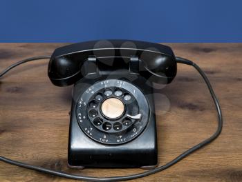 Old and antique rotary telephone on wooden desk with blue background