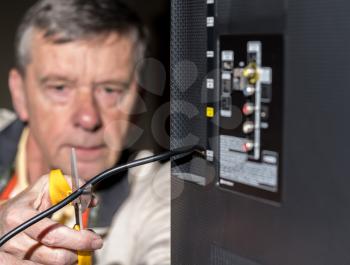 Close up of senior caucasian retired man cutting the aerial connection to his TV to illustrate cutting the cord