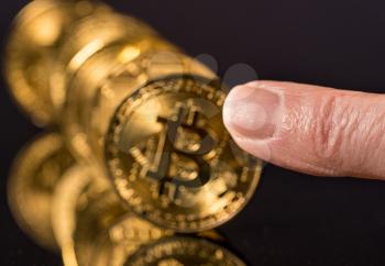 Bitcoin coins in a row on reflective surface with finger about to push them