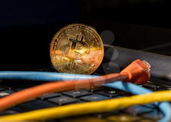 Single bitcoin coin standing on the keyboard of modern laptop computer
