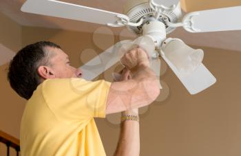 Senior adult male changing a bulb in a ceiling fan and lighting fixture