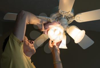 Senior adult male dusting the glass shade of a bulb in a ceiling fan and lighting fixture