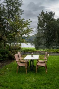 Table and four chairs on lawn by lake on a cold and wet day in Norway