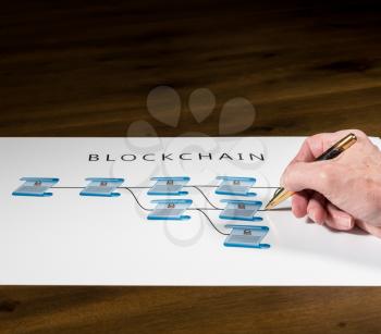 Blockchain schematic on printout on desk with senior technology executive pointing at one of the encrypted blocks of blockchain