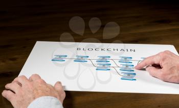Blockchain schematic on printout on desk with senior technology executive pointing at one of the encrypted blocks of blockchain