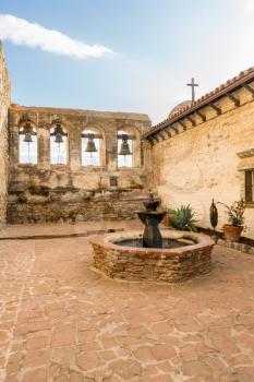 Bells in bell tower surround paved patio at San Juan Capistrano mission