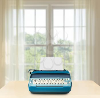 Concept image of working from home with electric typewriter on desk in front of bright summer window onto garden