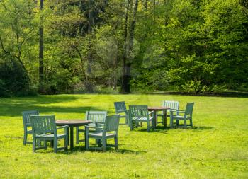 Teak garden tables and chairs in a large expansive garden with trees in background