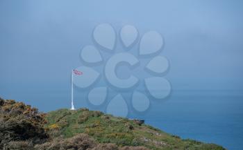 Union Jack flag on flagpole on hilltop cliff with the sea or ocean in the background