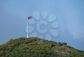 Union Jack flag on flagpole on hilltop cliff with blue sky in background
