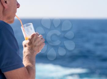 Senior caucasian adult man with tequila sunrise in glass on teak balcony rail of ocean cruise ship