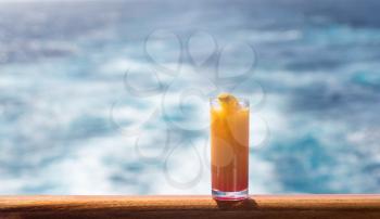 Tequila sunrise in glass on teak balcony rail of ocean cruise ship