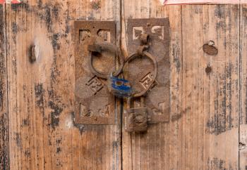 Rusty padlocks link the circular iron handles on wooden doors in ancient chinese doorway