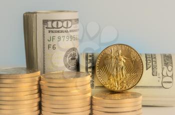 Stacks of pure gold eagle coins in front of rolled bankrolls of USA dollar bills
