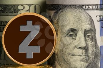 Macro single gold Zcash coin in front of rolled bankrolls of USA dollar bills with focus on Benjamin Franklin