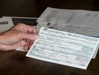 Senior hand holding Form 1040 Simplified for 2018  which allows for filing on April 15, tax day, on a postcard