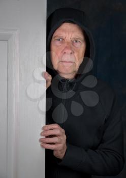 Senior retired caucasian man greeting someone to his home through doorway with worried expression