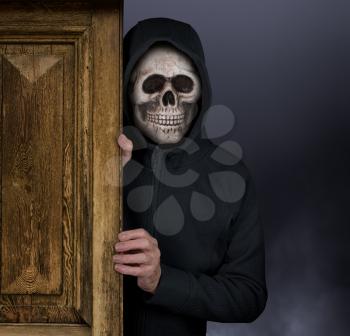 Halloween theme of man with skull in entrance doorway with storm behind welcoming visitors to haunted house