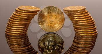 Single bitcoin coin reflected in glass surface to give illusion of being surrounded by ring of pure gold coins