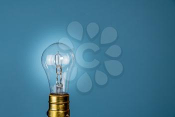 Halogen light bulb in holder set against a blue background with glow to illustrate EU decision to ban them