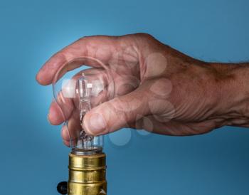 Senior caucasian man unscrewing a halogen lightbulb as concept for EU decision to ban the light bulbs