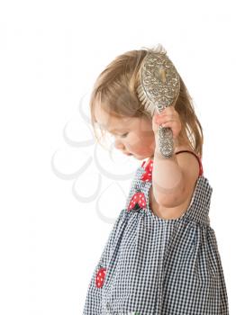 Young smiling caucasian toddler girl brushing blonde hair with silver brush and isolated against white
