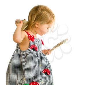 Young smiling caucasian toddler girl brushing blonde hair with silver brush and looking into mirror. Isolated against white