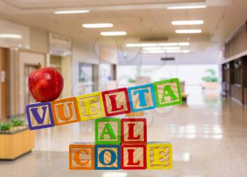 Vuelta al Cole translates to Back to School in spanish with wooden blocks with red apple on top. Background is a school entrance or corridor