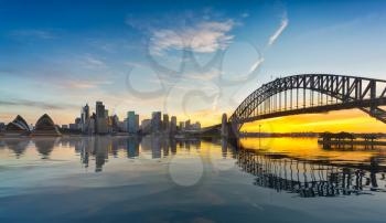 Dramatic widescreen panoramic image of the city of Sydney at sunset including the Rocks, Bridge and Opera House with an artificial reflection for the ocean