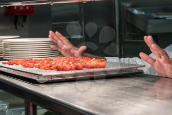 Chef preparing grilled tomatoes  in commercial stainless steel kitchen in restaurant