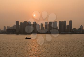 Sun rising in the distance over city skyline of large tower blocks of Qingdao in China